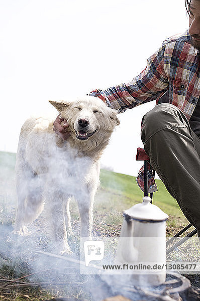 Ausgeschnittenes Bild eines Mannes  der einen Hund am Lagerfeuer streichelt