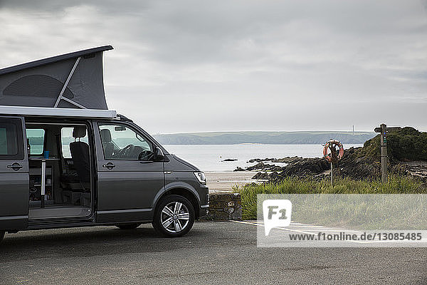 Motor home parked on road by beach against cloudy sky