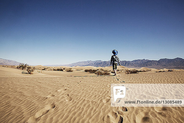 Rear view of boy walking at desert against clear blue sky