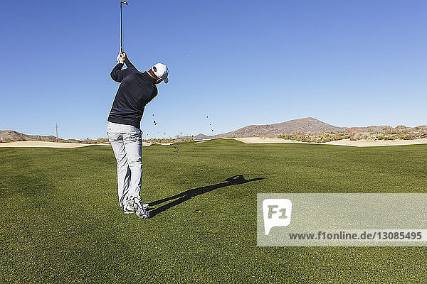 Rear view of golfer playing golf against on field against clear blue sky