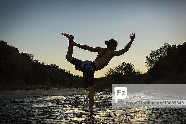 Scherenschnittmensch praktiziert Yoga am Seeufer bei Sonnenuntergang
