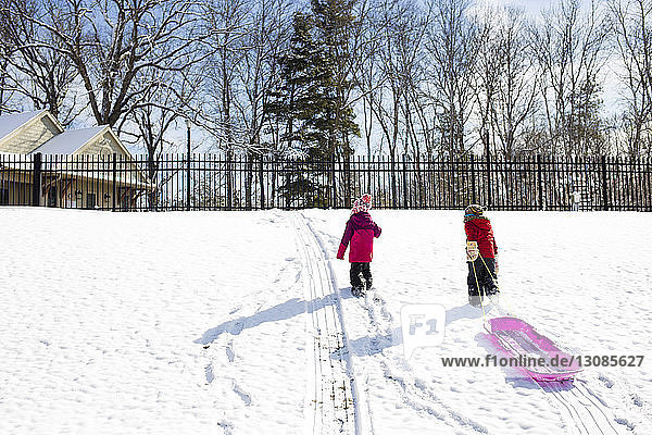 Brother pulling sled while walking with sister on snowy field