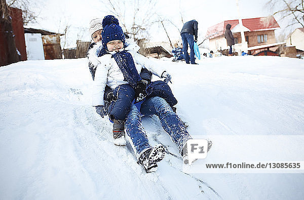 Excited mother and daughter tobogganing on snowy field