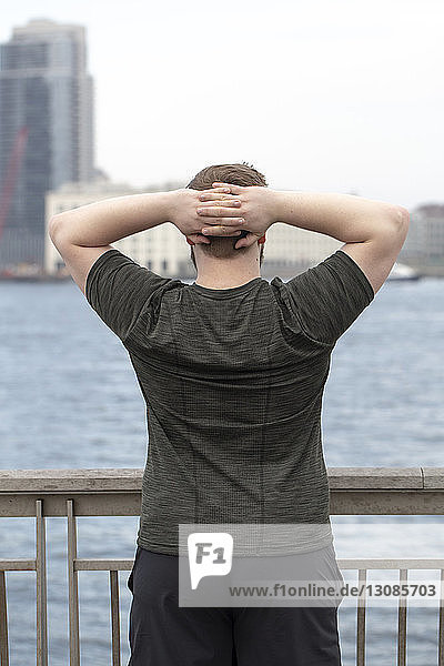 Rückansicht eines übergewichtigen Mannes mit Händen hinter dem Kopf  der auf einer Brücke am Fluss in der Stadt trainiert