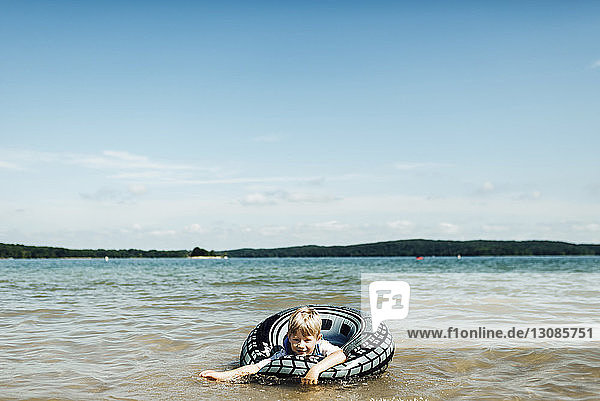 Junge im aufblasbaren Ring spielt im See gegen den Himmel
