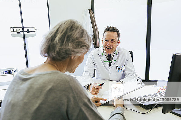 Happy doctor discussing with patient while sitting against wall at hospital