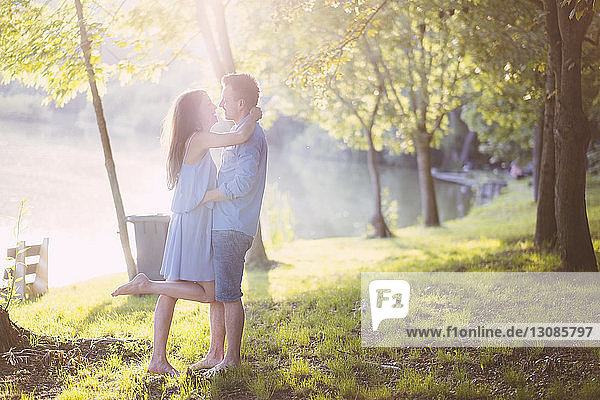 Seitenansicht eines romantischen Paares  das sich umarmt  während es auf einem Grasfeld im Park steht