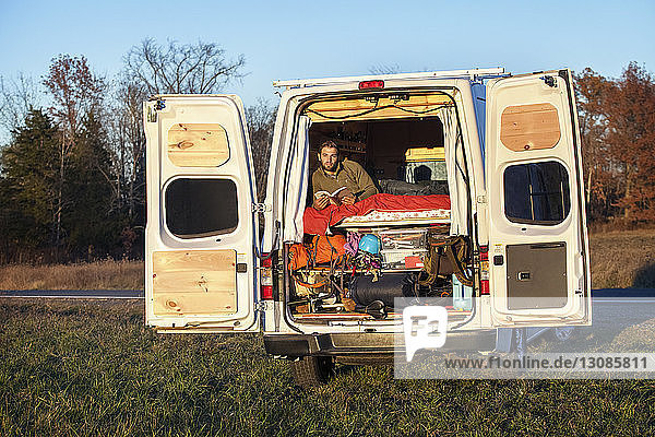 Man with book looking away while relaxing in camper van