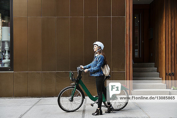 Frau geht mit dem Fahrrad auf dem Bürgersteig am Gebäude entlang