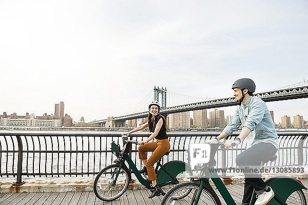 Glückliches Paar radelt auf Fußweg an der Manhattan-Brücke gegen den Himmel