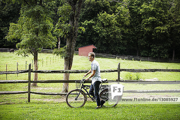 Man with bicycle walking by fence in farm