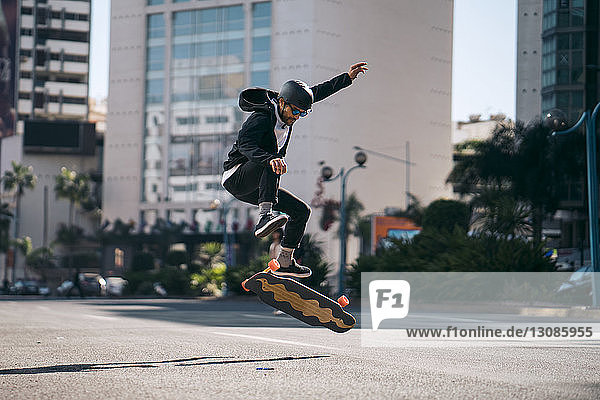 Mann in voller Länge  der beim Skateboarden auf der Straße in der Stadt einen Stunt vorführt