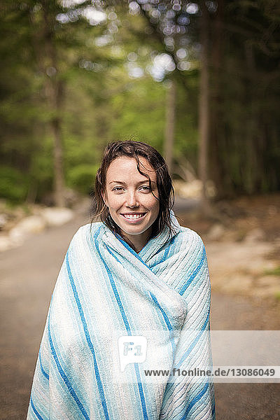 Porträt einer lächelnden  in eine Decke gehüllten Frau  die auf einer Straße im Wald steht