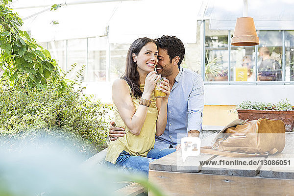Glückliche Frau hält ein Saftglas in der Hand  während sie mit einem Mann im Straßencafé sitzt