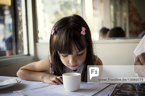 Girl looking in cup on table while sitting in restaurant
