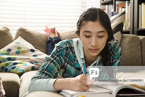 Teenage girl doing homework while lying on couch at home