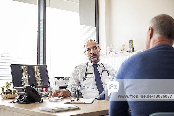 Arzt spricht mit Patient  während er im Krankenhaus am Schreibtisch sitzt