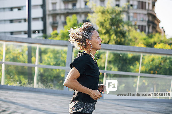Seitenansicht einer Frau  die beim Joggen an der Brücke Musik hört