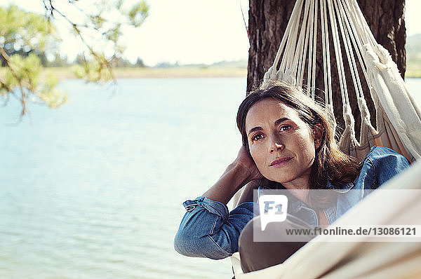 Nachdenkliche Frau schaut weg  während sie sich auf einer Hängematte am See entspannt