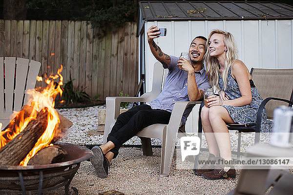 Friends taking selfie while sitting on chairs at yard