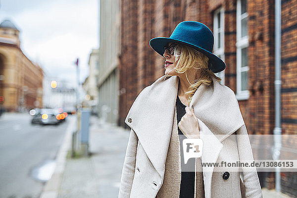Frau im Mantel schaut weg  während sie auf einem Fußweg in der Stadt steht