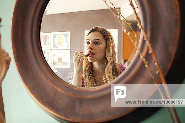 Frau trägt Lippenstift auf  während sie zu Hause in den Spiegel schaut