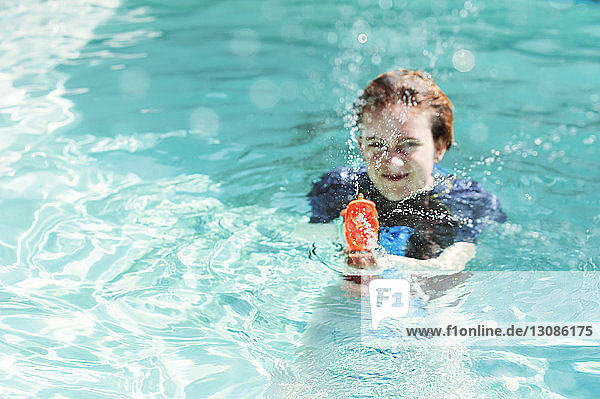 Portrait of teenage girl playing with squirt gun in swimming pool