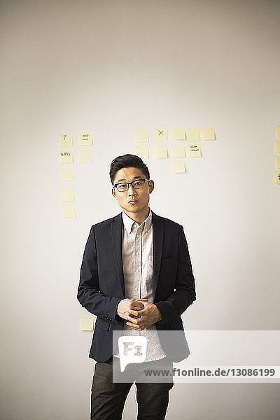 Portrait of confident businessman standing against wall in creative office