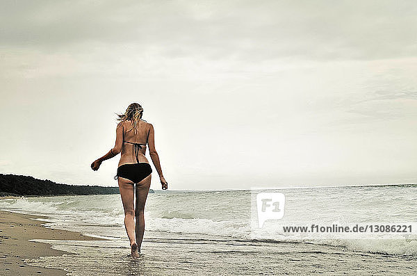 Rear view of woman wearing bikini walking at beach against clear sky