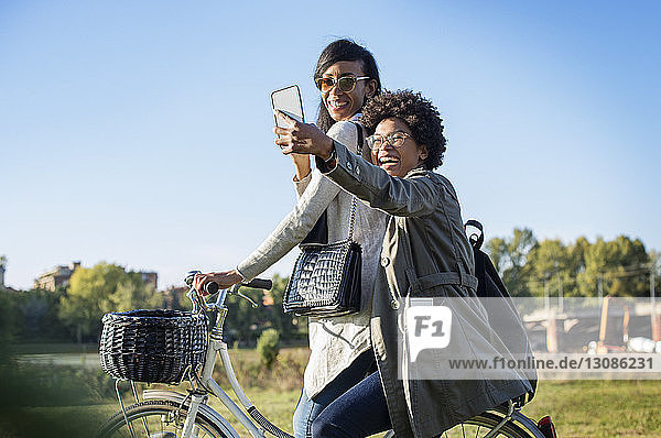 Glückliche Freunde  die beim Fahrradfahren auf dem Feld Selbsthilfe durchs Telefon nehmen