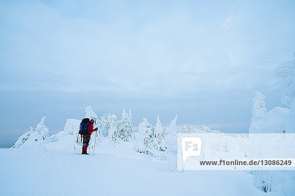 Seitenansicht eines Wanderers  der auf einer schneebedeckten Aufschüttung vor bewölktem Himmel steht