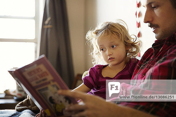 Tochter betrachtet Buch  während sie neben dem Vater im Bett sitzt