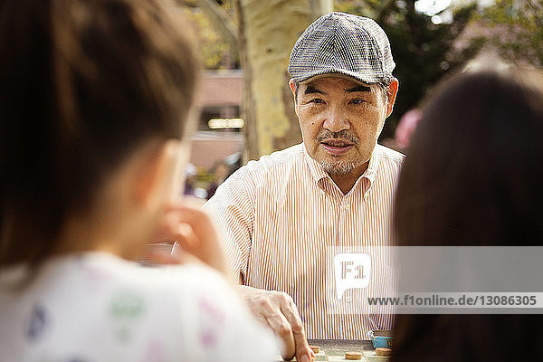 Großvater spielt Dame  während er im Park am Tisch sitzt