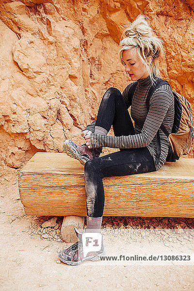 Frau schnürt Schuhschnürsenkel  während sie auf einer Bank vor Felsformationen sitzt