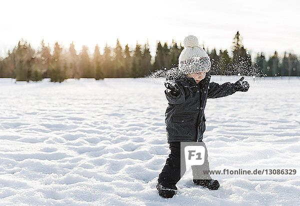 Boy playing on snow covered field against sky