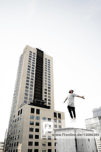 Niedrigwinkelansicht eines Mannes  der bei klarem Himmel auf die Gebäudeterrasse springt