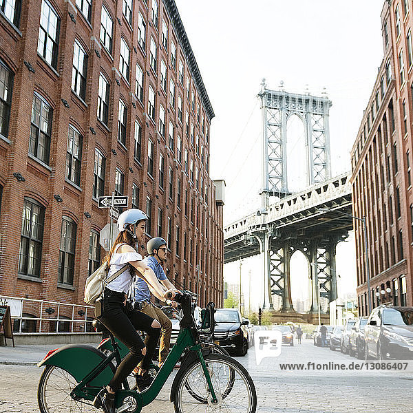 Ein Paar radelt auf der Straße an Gebäuden in der Stadt vorbei gegen die Manhattan-Brücke