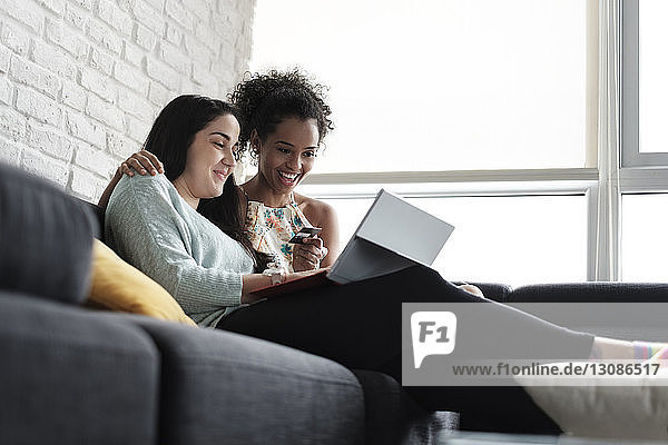 Niedriger Blickwinkel auf ein glückliches lesbisches Paar beim Online-Shopping  während es zu Hause auf dem Sofa sitzt