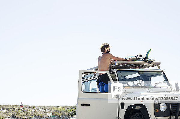Man taking surfboard from car roof against clear sky during sunny day