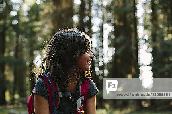 Glückliches Mädchen mit Rucksack schaut weg  während sie im Wald sitzt