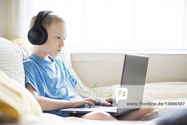 Junge hört Musik  während er zu Hause einen Laptop benutzt