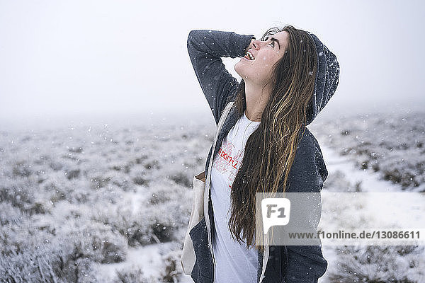 Woman with long hair looking up while standing on snow covered field