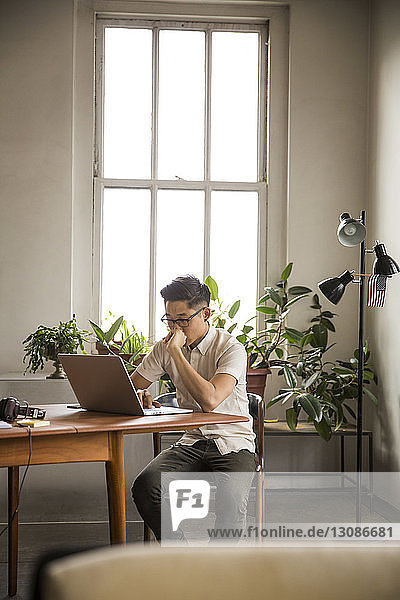 Geschäftsmann mit Laptop  während er im Kreativbüro am Tisch gegen das Fenster sitzt