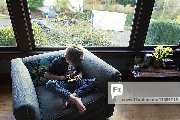 Hochwinkelansicht eines Jungen  der auf einem Sessel sitzend ein Spiel auf einem Mobiltelefon spielt
