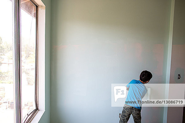 Rückansicht eines Jungen  der zu Hause eine Wand mit einem Farbroller bemalt
