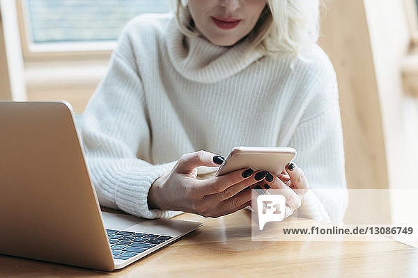 Midsection of woman using mobile phone while sitting by table at home