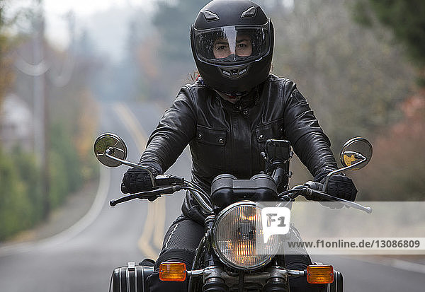 Female biker wearing crash helmet while riding motorcycle on road