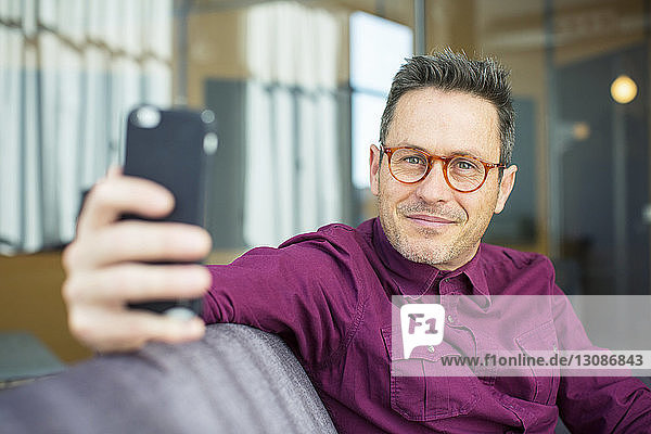 Porträt eines Geschäftsmannes  der ein Mobiltelefon benutzt  während er im Büro auf dem Sofa sitzt
