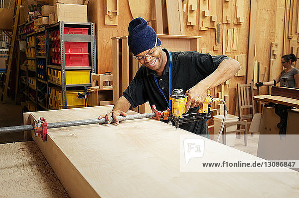 Fröhlicher Zimmermann bohrt Holzbohlen in der Werkstatt