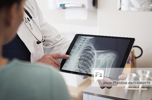 Mittelteil des Arztes  der dem Patienten im Krankenhaus ein Röntgenbild auf einem Tablet-Computer zeigt